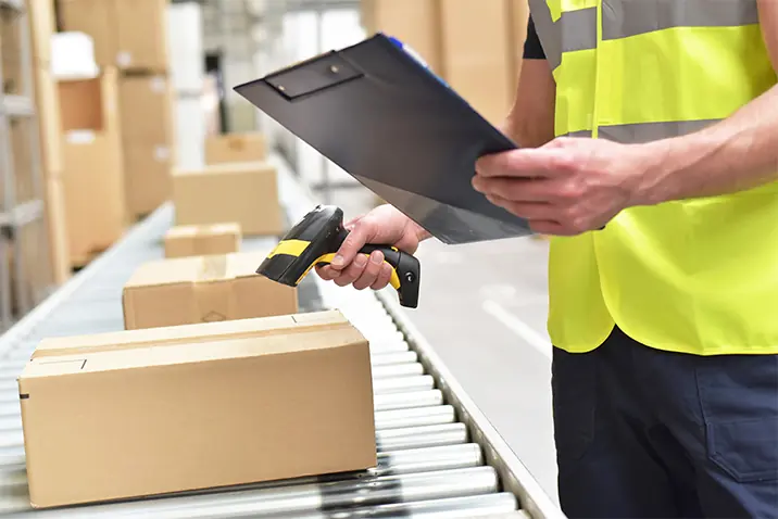 Person scannt ein Paket in einer Lagerhalle mit Handscanner und Checkliste.