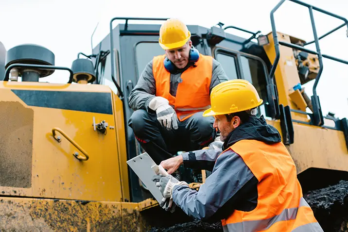 Zwei Personen stehen vor einem Bagger auf einer Baustelle
