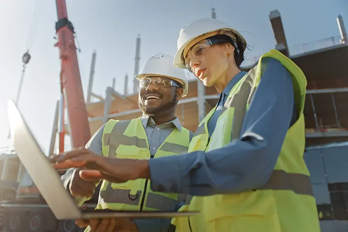 Zwei Personen nutzen ein Notebook zur Abstimmung auf der Baustelle