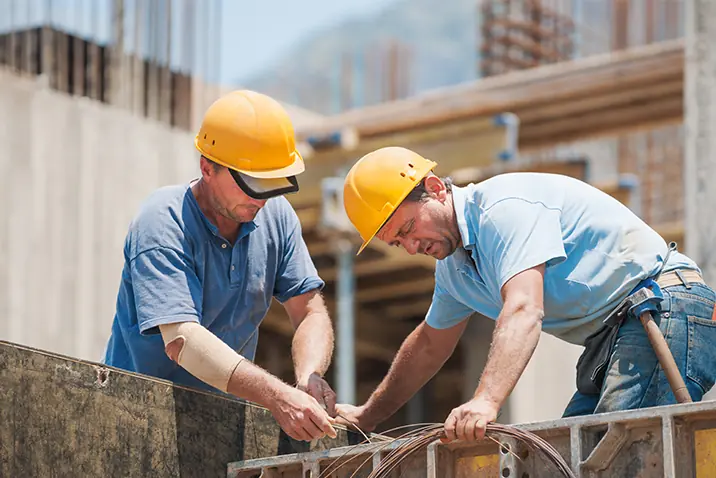 Zwei Personen mit Schutzhelmen arbeiten gemeinsam an einer Schalung auf einer Baustelle