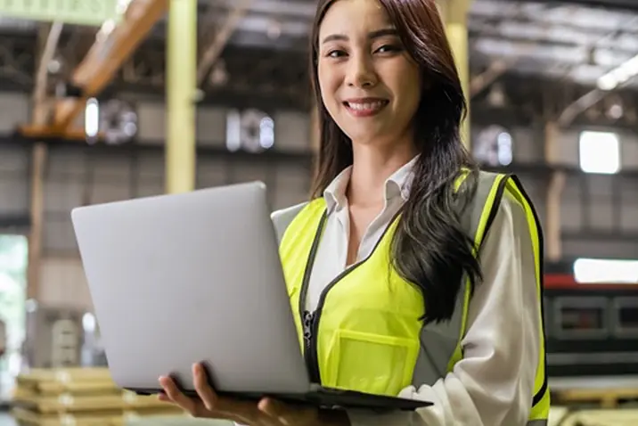 Person in Schutzweste nutzt ein Notebook in einer Industriehalle