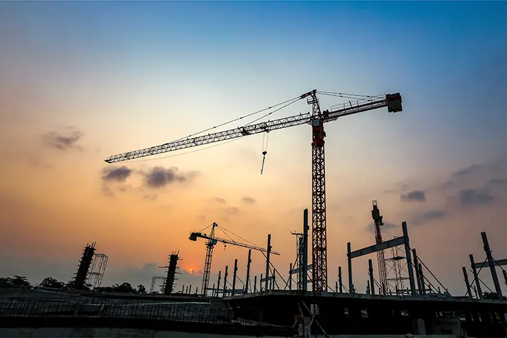 Mehrere Baukräne auf einer Baustelle bei Abendlicht