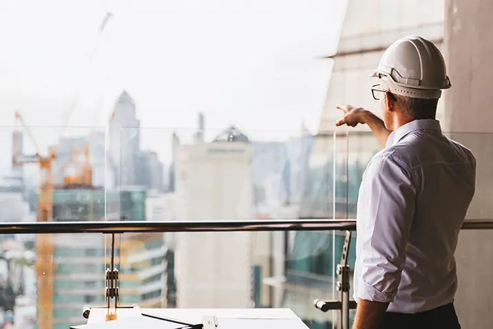 Person mit Schutzhelm steht auf einem Balkon eines Rohbaus