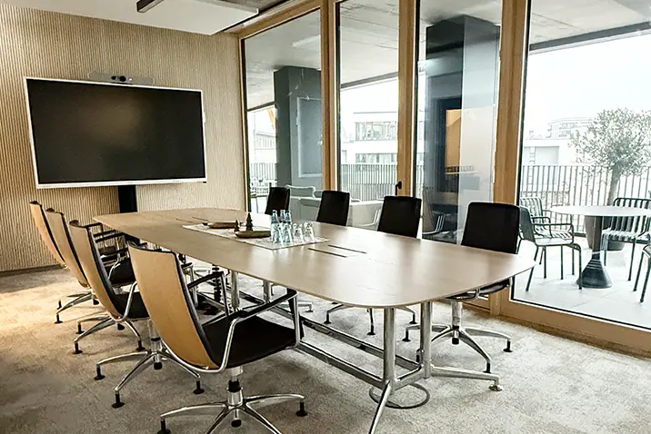 Konferenzraum mit großem Tisch, Stühlen und Präsentationsbildschirm