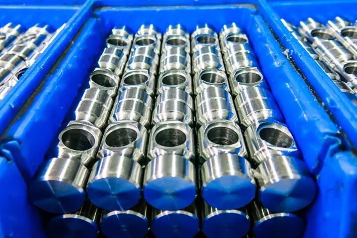 Metallische Drehteile liegen sortiert in einer blauen Kunststoffkiste