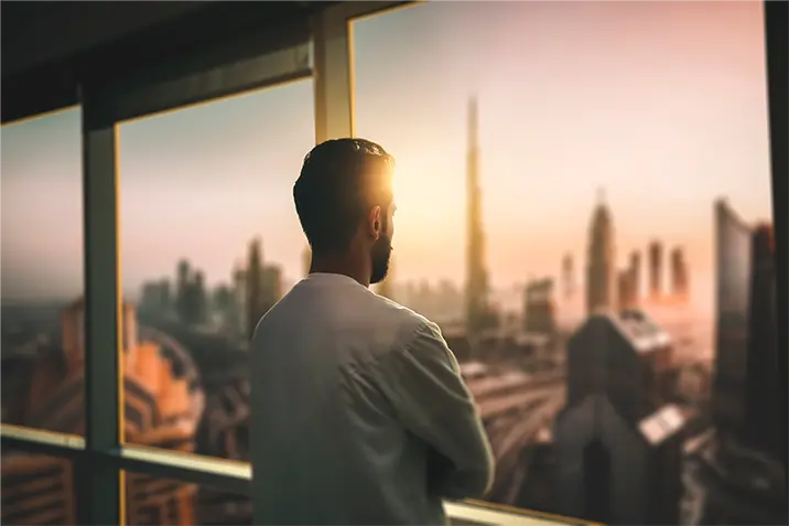 Person blickt aus dem Fenster eines modernen Bürogebäudes auf eine Stadtansicht