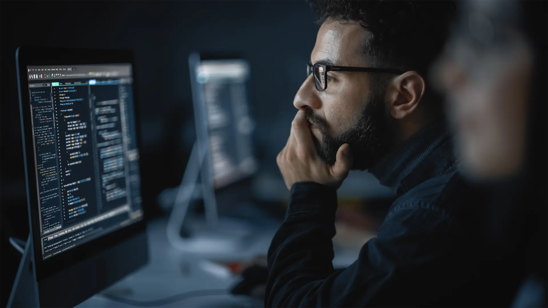 Person arbeitet konzentriert an einem Computer mit geöffnetem Code-Editor 