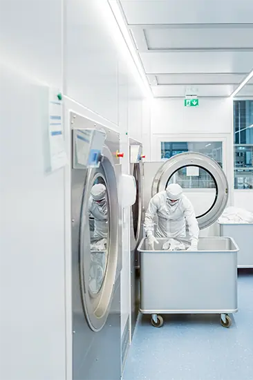 Mitarbeitende in hygienischer Schutzkleidung beim Beladen industrieller Waschmaschinen