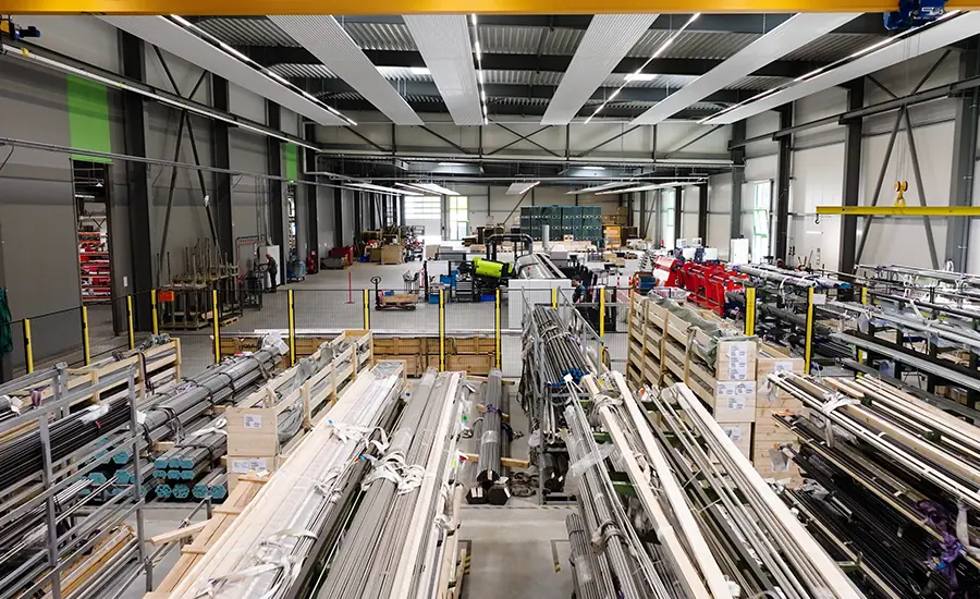 Großzügige Produktionshalle mit gelagerten Metallrohren und automatisierten Fertigungslinien