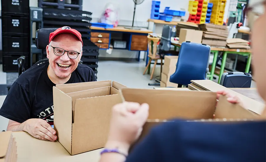 Person arbeitet an einer Verpackungsstation mit Kartonagen in einer Werkstatt